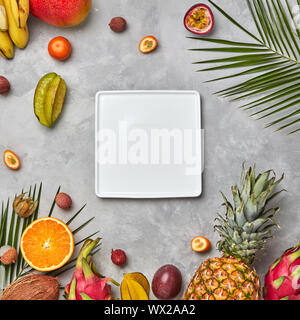 Quadratische weiße leere Platte nalmium Blätter und Früchte, saftig Trio kumkva, Physalis, Passionsfrucht, Banane auf grauem Beton backgr Stockfoto