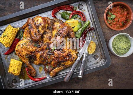 Spatchcocked Grill hähnchen Al mattone Chili mit chimichurri Sauce und Chilli relish als Draufsicht auf ein altes Blech Stockfoto