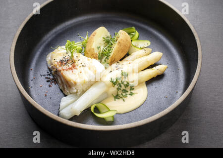 Moderne Deutsche Frittierter Kabeljau Filet mit weißen Spargel in Sauce Hollandaise und gebratenen Kartoffeln als Draufsicht auf einer Platte Stockfoto