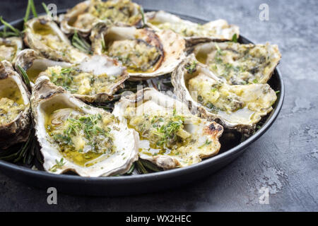 Grill overbaked frische Austern mit Knoblauch und Kräutern aus nächster Nähe auf einer Platte angeboten geöffnet Stockfoto