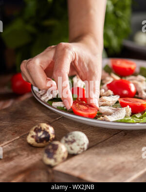 Frau hand Tomate cherry zu einem Keramik Teller mit frischem Salat mit Zutaten aus biologischem Anbau auf einem Holztisch. Gesunde Ernährung Essen. Stockfoto