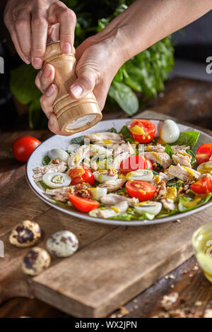 Weibliche hand salz hausgemachten frischen Salat aus natürlichen organischen Gemüse, Fleisch, Wachtel egss auf einem Holztisch. Stockfoto