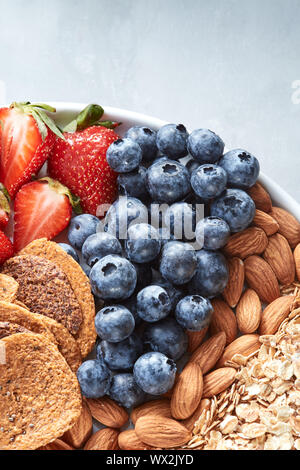 Frische reife Früchte, Blaubeere, Mandel Nüssen, Haferflocken, Chips auf einem Schild auf einem grauen Hintergrund. Stockfoto