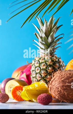 Gruppe von exotischen und tropischen Früchten. Mango, Drachenfrucht, Passionsfrucht, Kokosnuss, Ananas, Karambolen, kumquat auf einem blauen Hintergrund Stockfoto