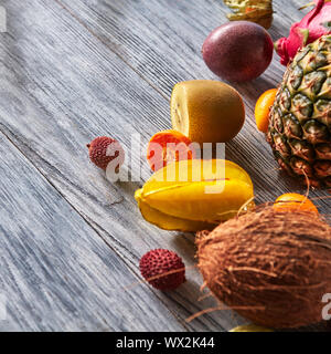 Tropische Komposition aus exotischen Früchten mit Reife Ananas, karambola, Mango, Passionsfrucht auf einem grauen Hintergrund, aus Holz Stockfoto