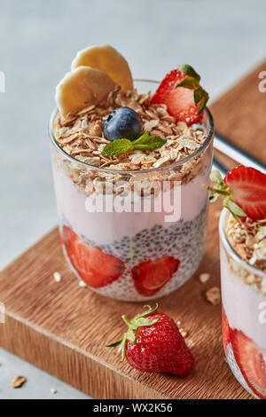 Glas Obst Smoothie und frische Beeren mit Oat hausgemachtes Müsli, Chia Samen auf einem Holzbrett auf einem grauen. Stockfoto