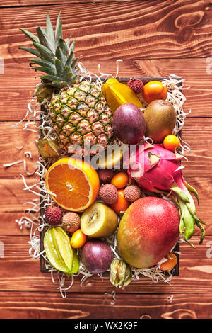 Die box mit exotischen und tropischen Früchten - frische reife Ananas, Mango, Drachenfrucht, Orange, Karambolen, Kiwi auf einem Holztisch, plac Stockfoto