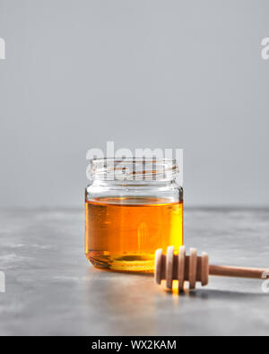 Honig in einem Glas mit Holzstab auf grauem Stein Tabelle. Jüdische Rosch Haschanah Urlaub. Stockfoto