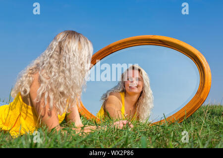 Junge blonde Frau im Gras liegend mit Spiegel Stockfoto