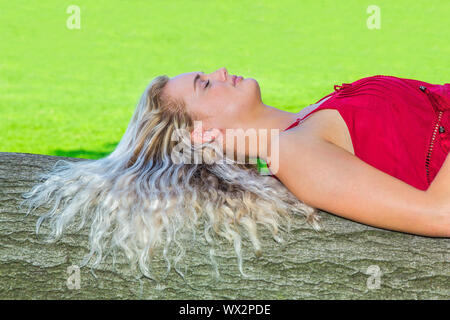 Junge Frau mit langen Haaren liegt auf Baumstamm Stockfoto