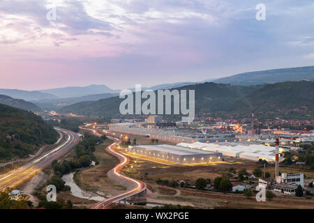 Blick von oben auf ein großes, modernes, aufhellen Fabrik, alten, verfallenen Fabrik, kurvenreiche Straße mit Brücke und Auto Wanderwege Stockfoto