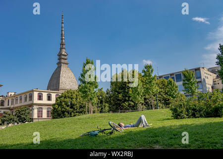 Eine Person, die auf dem Gras mit Der Kuppel und dem Turmspitze der Mole Antonellana liegt, im Hintergrund ein architektonisches Symbol der Stadt Turin, Italien Stockfoto