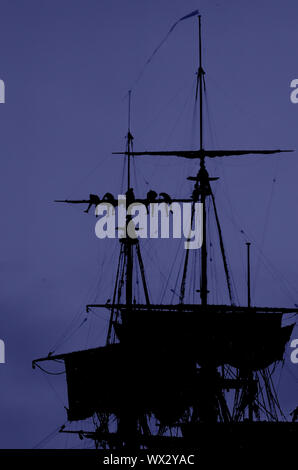 Ein lila Himmel silhouette Foto von Matrosen arbeiten an der Takelage eines modernen Segelschiff (Abschleppen/Senken der Segel) in der Dämmerung während des Besuchs des Bemühen, Whitby, Yorkshire, England im Jahr 2000. Stockfoto