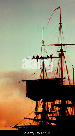 Eine silhouette Foto von Matrosen arbeiten an der Takelage eines modernen Segelschiff (Abschleppen/Senken der Segel) während des Abends während des Besuchs des Bemühen, Whitby, Yorkshire, England im Jahr 2000. Stockfoto