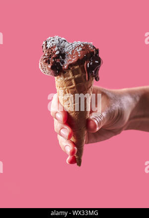 Die Hand eines Mannes hält eine Waffel Kegel mit Obst, Eis mit Kokos Chips auf einem rosa Hintergrund mit Kopie Raum eingerichtet. Stockfoto