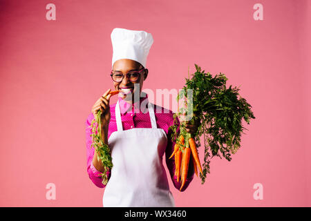 Lächelnd cook Holding Karotten, beißen in eine Stockfoto