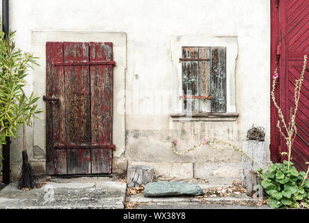 Alten rustikalen Vintage House front mit massiven hölzernen Tür und Fensterläden und Blumen an den Seiten Stockfoto