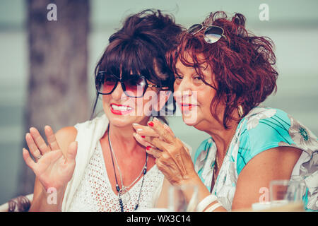 Bild eines zwei Glückliche älterer Frauen Freunde im Cafe sitzen Sprachen miteinander Kaffee trinken, Pointing Finger zu empfehlen. Stockfoto