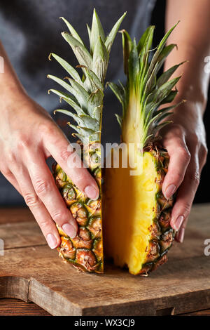 Die beiden Hälften des Ripe bio Ananas halten die Hände des Mädchens auf einem alten Holz- Board. Exotische Früchte Stockfoto