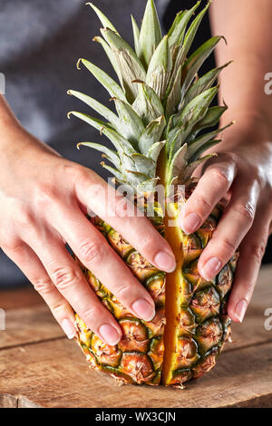 Frische Hälften einer exotischen Ananas halten die Hände der Mädchen auf einer Küche aus Holz. Vitamin Obst Stockfoto