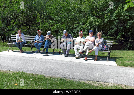 Sieben Leute, eine jüngere und ältere, teilen Parkbänke im kulturellen Gärten von Rockefeller Park in Cleveland, Ohio, USA. Stockfoto