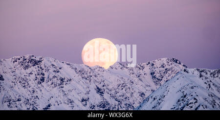 Vollmond in einen rosa Himmel steigen in einer winterlichen Bergwelt Stockfoto