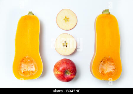 Zwei Hälften eines Kürbis mit in Scheiben geschnittenen und ganze Äpfel auf einem weißen Hintergrund. Stockfoto