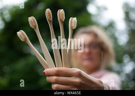 Junge schöne Frau mit blond gelocktem Haar in Rosa hipster Jacke und Brille Holding fünf Bambus Zahnbürsten in die Hand. Null Abfall Konzept Stockfoto