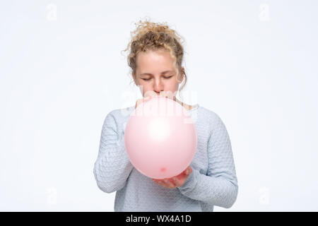 Junge kaukasier curly Frau in gblue sweateris Blasen pink Balloon Vorbereitung für die Geburtstagsparty. Studio shot Stockfoto