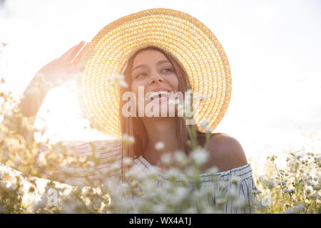 Schöne braunhaarige Frau in Weiß einstellen ihren Hut sitzen unter Feld Blumen Stockfoto