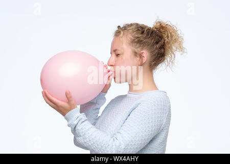 Junge kaukasier curly Frau in gblue sweateris Blasen pink Balloon Vorbereitung für die Geburtstagsparty. Studio shot Stockfoto