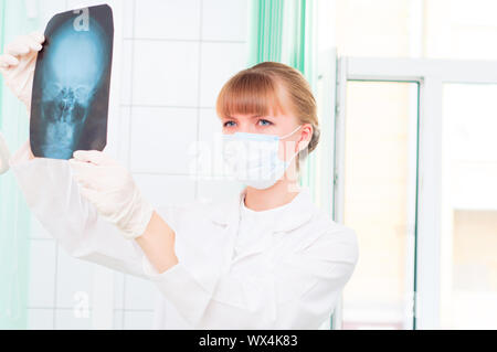 Junge Frau in Schutzmaske dotstor schaut auf eine Röntgenaufnahme des Schädels Stockfoto