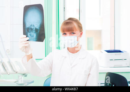 Junge Frau in Schutzmaske dotstor schaut auf eine Röntgenaufnahme des Schädels Stockfoto