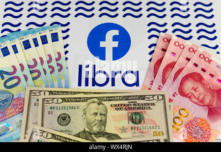 Facebook und die Waage Logos auf die Broschüre, die von US-Dollar, Euro und Chinesischen Renminbi Banknoten umgeben. Konzeptionelle Foto. Stockfoto