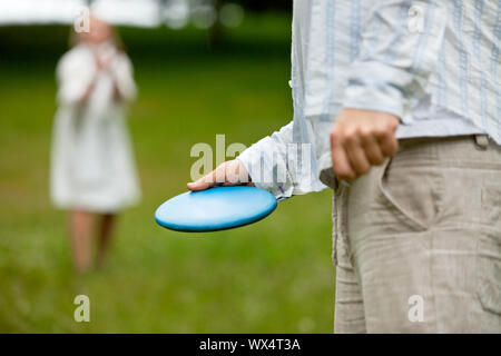 Mittelteil des Menschen in Freizeitkleidung bereit Frisbee mit Frau im Hintergrund zu werfen Stockfoto