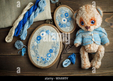 Zwei Stickereien in dekorative Rahmen, Zubehör für Stickereien und Teddybär Spielzeug auf Holz- Hintergrund Stockfoto