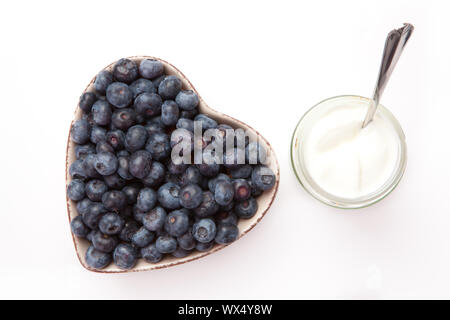 Joghurt und Heidelbeeren in eine herzförmige Schüssel vor einem weißen Hintergrund Stockfoto