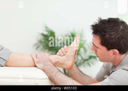Physiotherapeutin beim Massieren eines Fußes in einem Raum sitzen Stockfoto