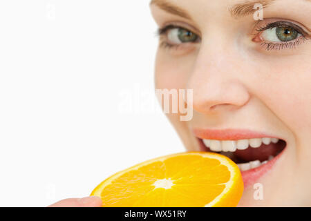 Nahaufnahme einer Frau eine Orangenscheibe im Mund vor weißem Hintergrund platzieren Stockfoto