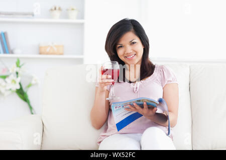 Frau mit einer Zeitschrift halten Sie ein Glas Rotwein in einem Wohnzimmer Stockfoto