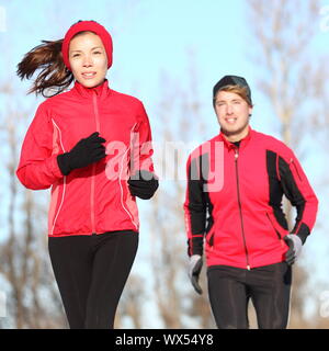 Gesunde Lebensweise winter läuft. Runner paar Joggen im City Park in warmen Winter Sport Kleidung. Passen asiatische Frau fitness Model und kaukasischen Mann m Stockfoto