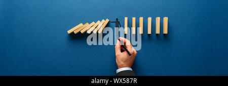 In der breiten Ansicht Bild der männlichen hand Zeichnung Silhouette eines Mannes einen Stop Geste Holz- Domino vor dem Einsturz zu verhindern. Über Marine blauen Hintergrund. Stockfoto