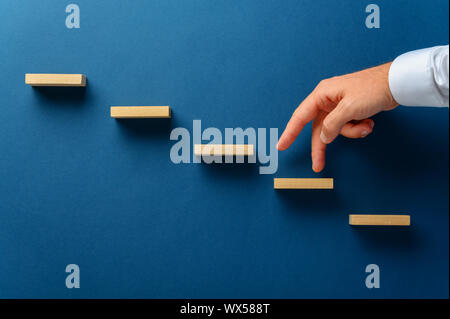 Geschäftsmann seinen Finger nach oben, eine Treppe aus Holz in einem konzeptionellen Bild. Über Marine blauen Hintergrund. Stockfoto