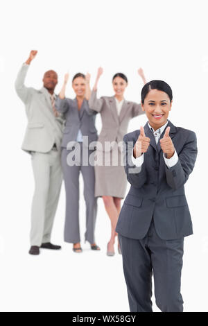 Verkäuferin mit Jubel Team hinter ihr geben Daumen bis vor einem weißen Hintergrund Stockfoto