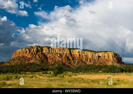 Mesa mit roten Felsen Sandstein Klippen über einer Wiese Wiese unter einem dramatischen stürmischen Himmel im Norden von New Mexico Stockfoto