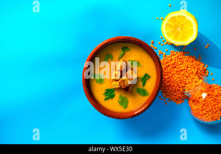 Frische Linsen creme Suppe in eine braune Schale auf blauem Hintergrund mit kopieren. Ansicht von oben. Linsen Grütze im Glas und frischer Zitrone. Stockfoto