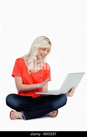 Schönen blonden Frau, die ihre rechte Hand winken vor ihrem neuen grau Laptop Stockfoto