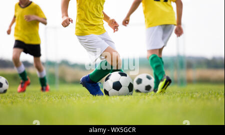 Fußball-Camp für Kids. Jungen Praxis Dribbling in einem Feld. Spieler entwickeln gute Fußball-Dribblings. Kinder, die in gelben Hemden Training mit Kugeln. Stockfoto