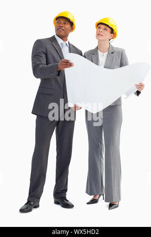 Ein Geschäftsmann und Frau das Tragen von Schutzhelmen und hält ein Papier sind auf der Suche nach oben Stockfoto