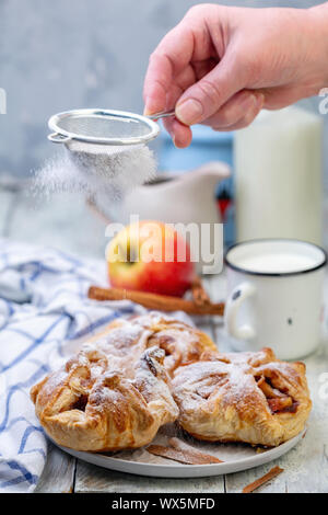 Puffs von Äpfeln und Zimt auf einer Platte bestreut mit Puderzucker. Stockfoto